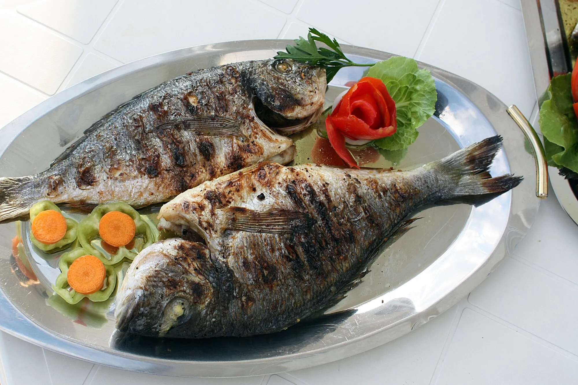 Two whole grilled fish on a platter with tomato and pepper garnish, a staple of Mediterranean cooking