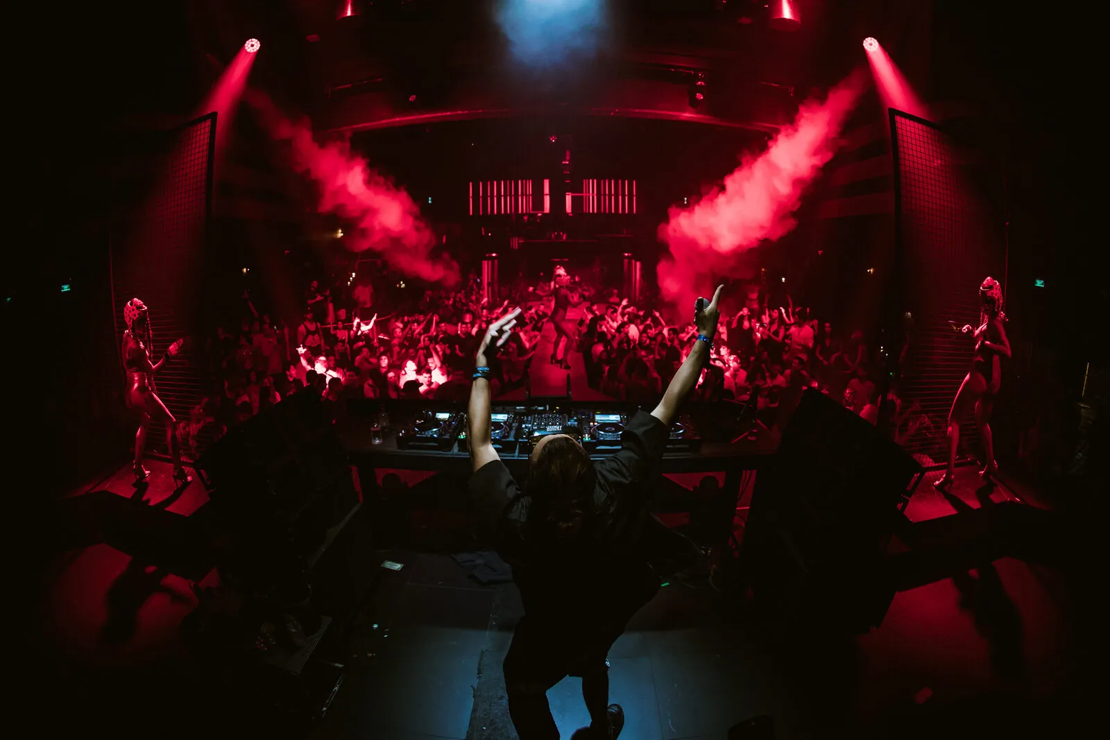 A DJ playing to a packed dancefloor under red lights at a club in Ibiza
